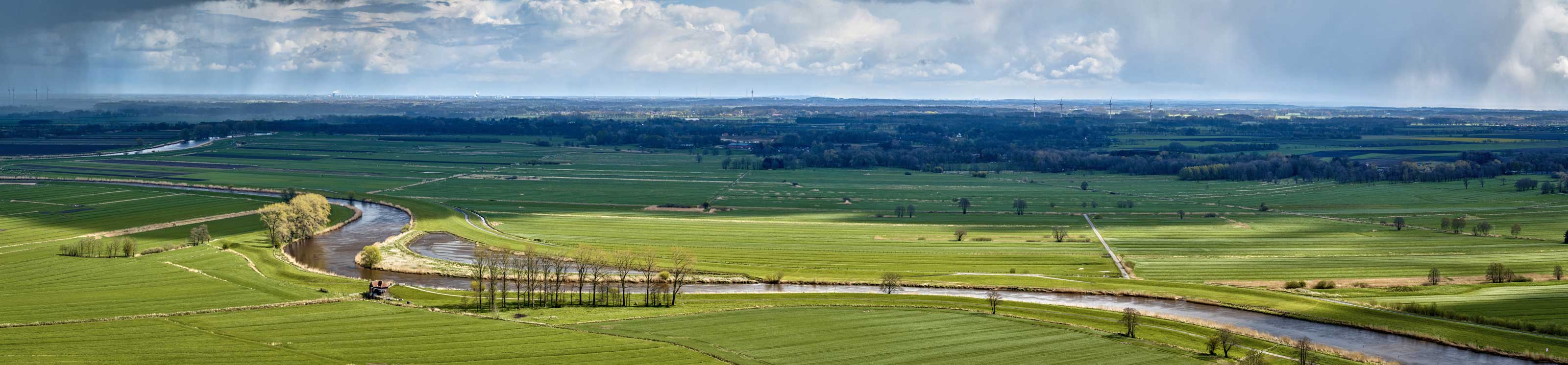 Luftbild über die Flusslandschaft der Oste nahe dem Ferienpark Geesthof mit Sonne und Regenwolken