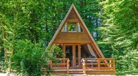 A-förmiges Holzferienhaus im Schatten unter Bäumen im Geesthof Ferienpark