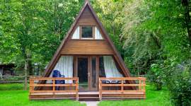 A-förmiges Holzferienhaus im Schatten unter Bäumen im Geesthof Ferienpark