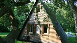 A-förmiges Holzferienhaus im Schatten unter Bäumen im Geesthof Ferienpark