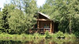 Blockhütte mit Veranda am Teich, umgeben von Bäumen