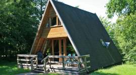 A-förmiges Holzferienhaus im Schatten unter Bäumen im Geesthof Ferienpark