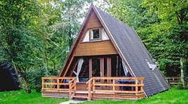 A-förmiges Holzferienhaus im Schatten unter Bäumen im Geesthof Ferienpark
