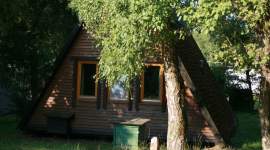 A-förmiges Holzferienhaus im Schatten unter Bäumen im Geesthof Ferienpark