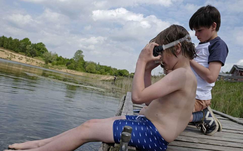 Foto eines Jungen mit Taucherbrille, der auf einem Steg am Wasser sitzt.