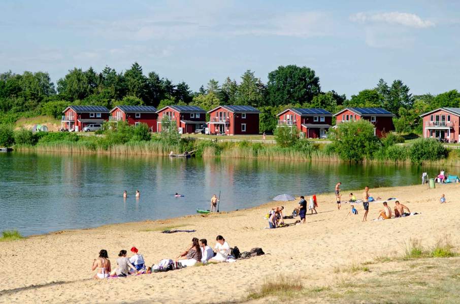 Foto eines Strandabschnitts am Geestsee mit Seehäusern im Hintergrund.