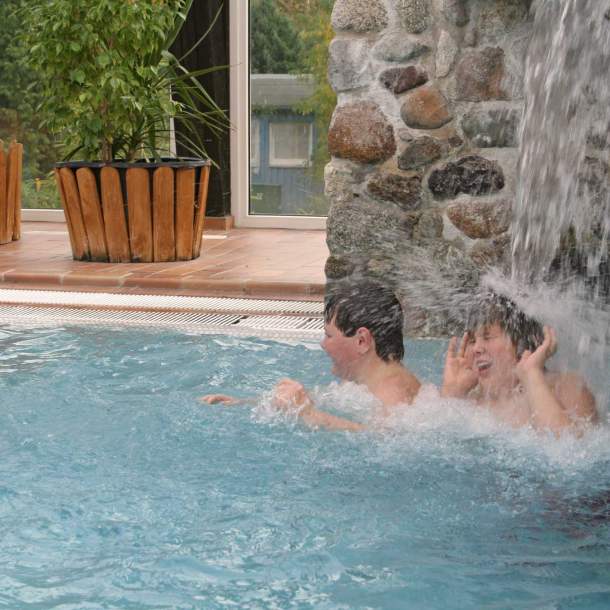 Foto von zwei Jungen, die unter einem Wasserfall im Schwimmbad stehen.