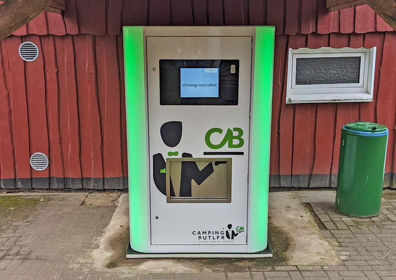 Foto vom Camping Butler, der am roten Sanitärgebäude aufgebaut steht.