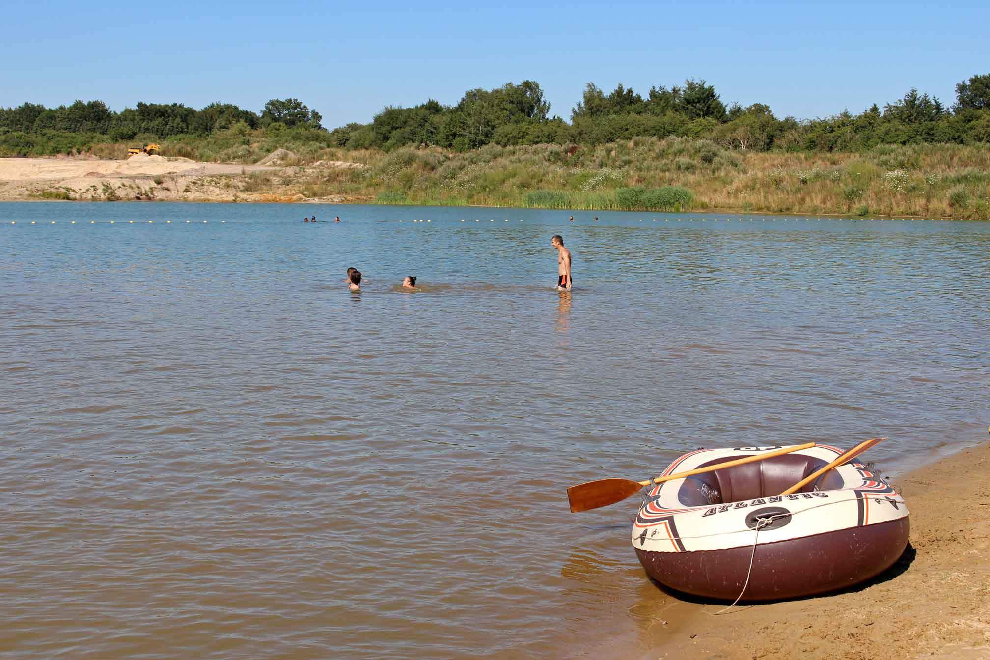 Foto vom Geestsee, in dem Menschen baden und ein Schlauchboot am Strand liegt.