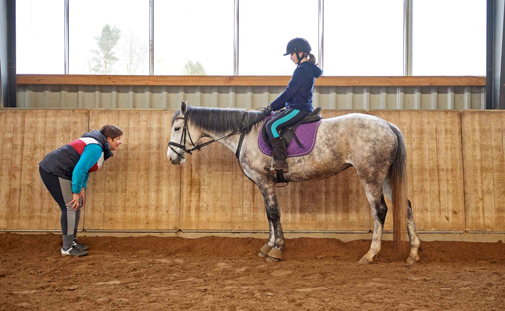 Foto von einem Kind auf einem Pferd, die in der Reithalle stehen.