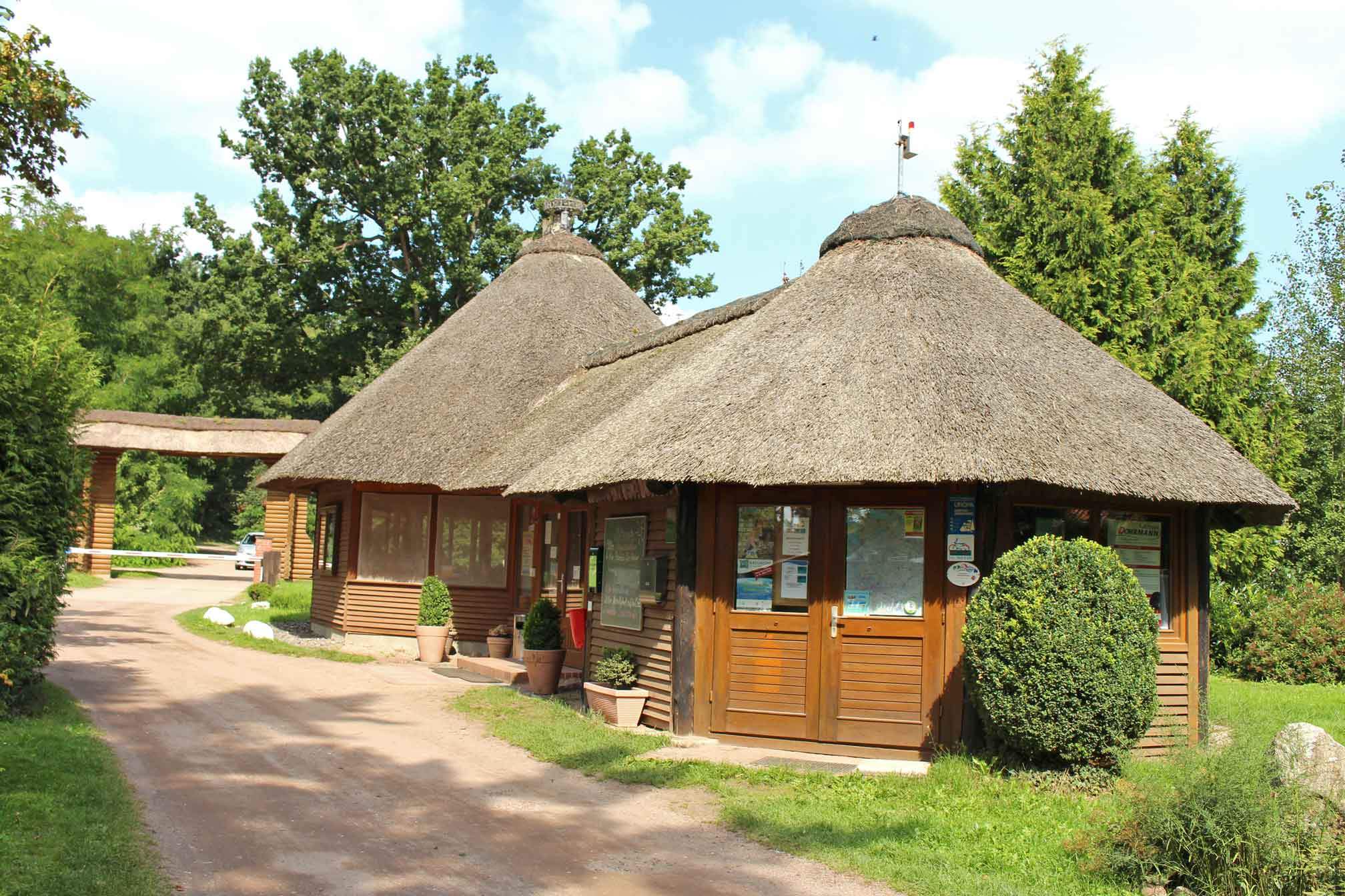 Foto von einem reetgedeckten Holzhäuschen, dass an einem Schotterweg steht.