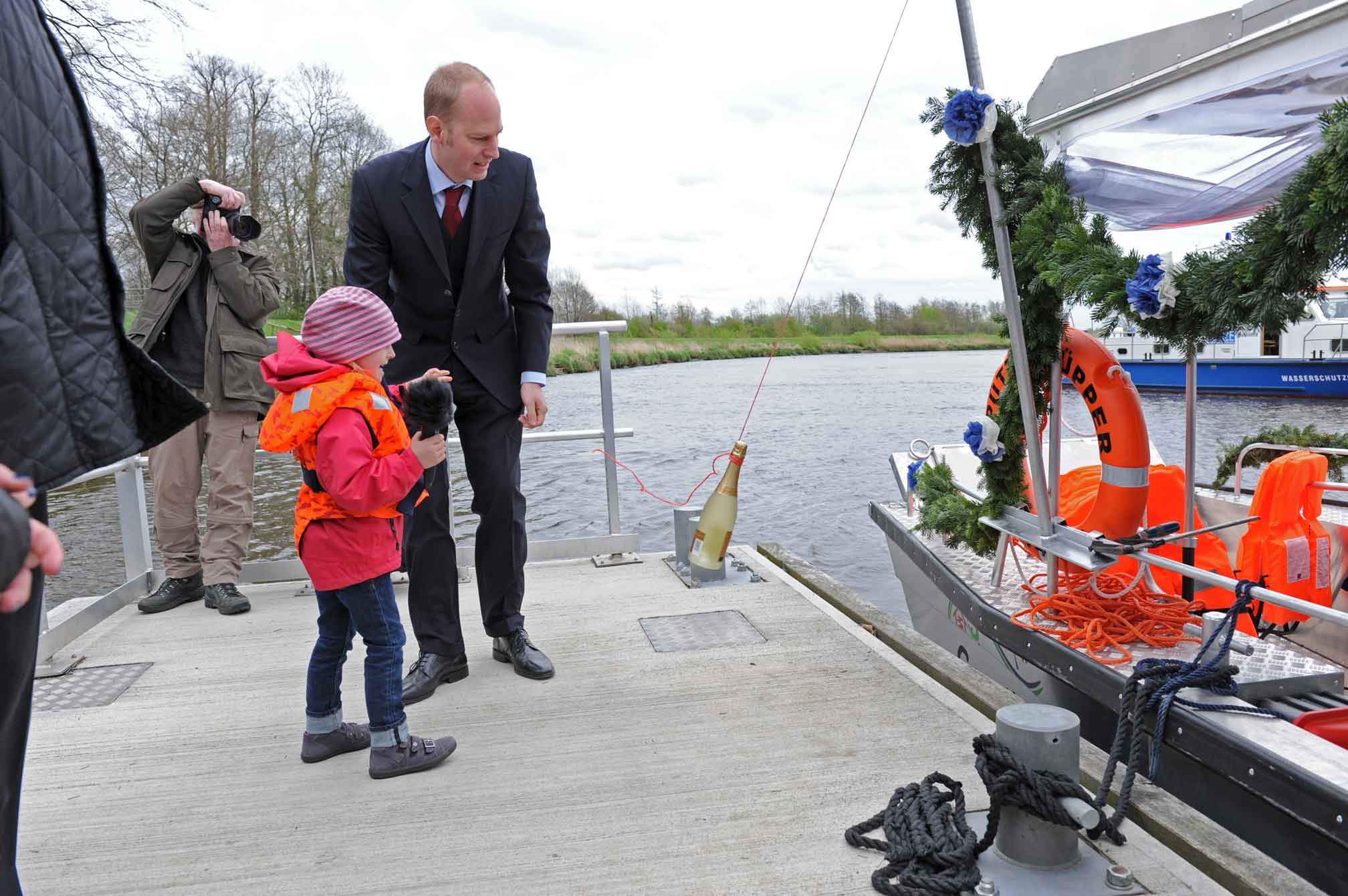 Foto von einem Mann im Anzug mit Kind in Schwimmwest, die eine Sektflasch an den Püttenhüpper schwingen.