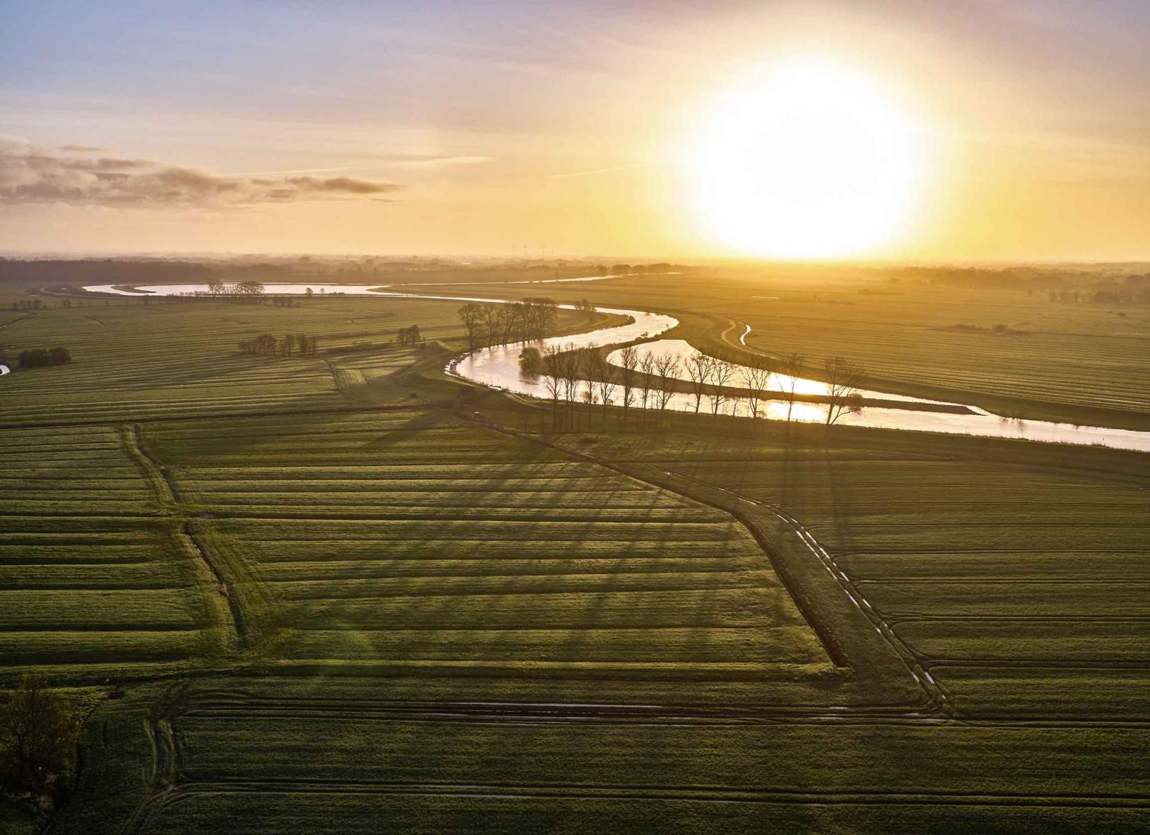 Foto eines Sonnenuntergangs über der Oste und einer kleineren Pütte