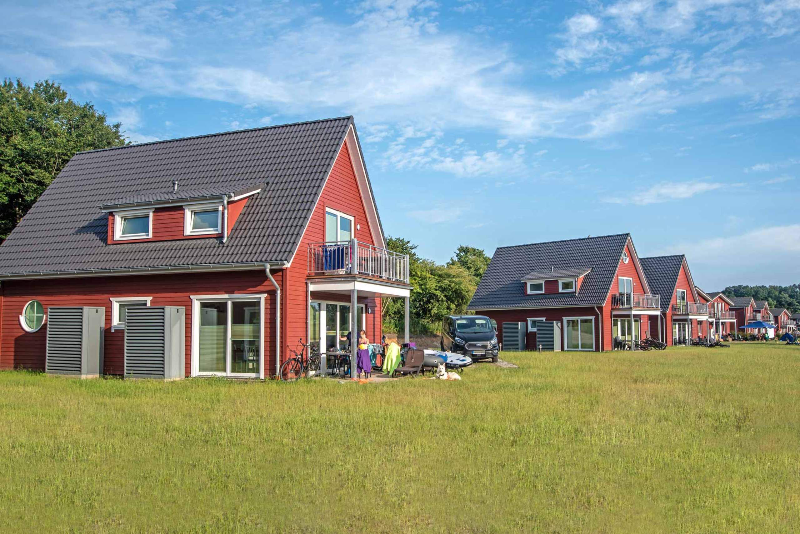 Rote Schwedenhäuser mit Rasenfläche und Gästen auf der Terrasse.
