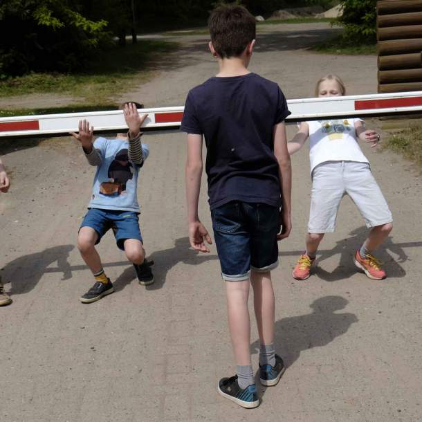 Foto von drei Kindern, die an einer Zufahrts-Schranke spielen.