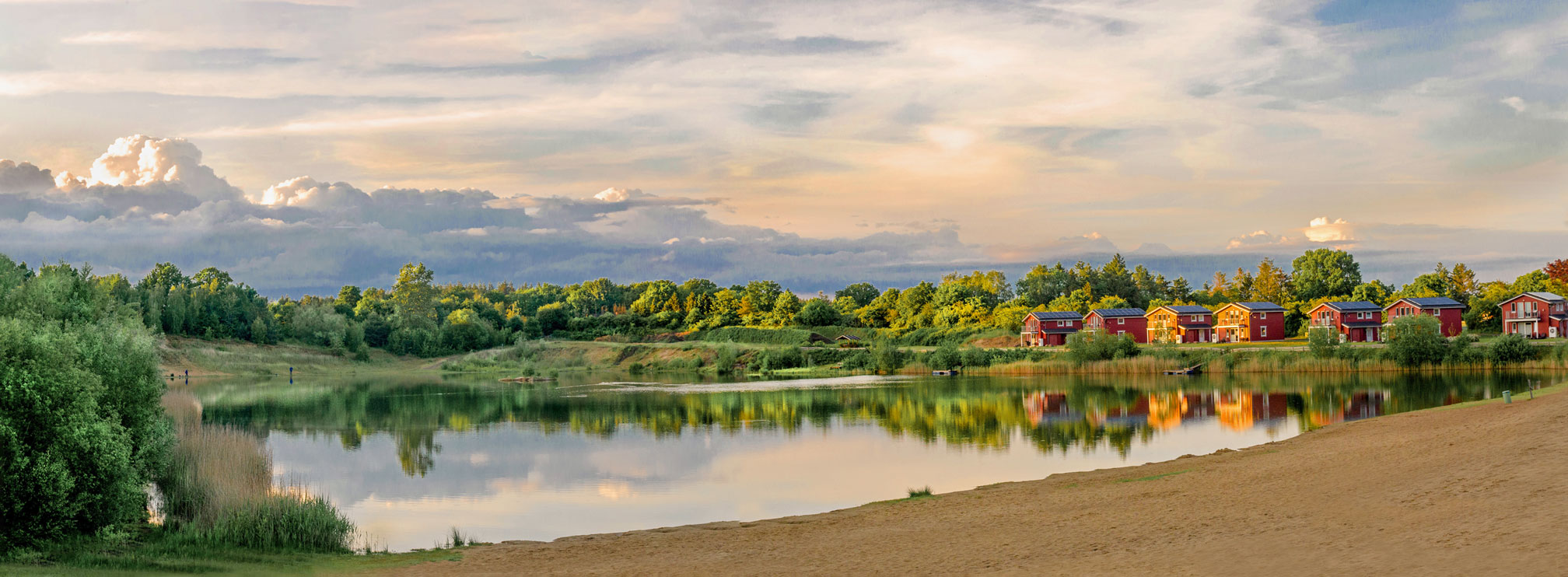 Außenansicht moderner Ferienhäuser im Schwedenstil am Geestsee, umgeben von grüner Natur mit blauem Himmel