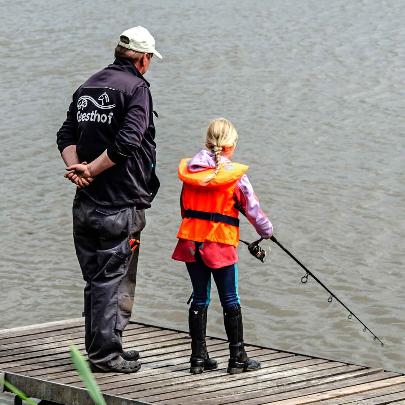 Foto von einem Mädchen und einem Angelguide, die auf einem Steg am Wasser stehen.