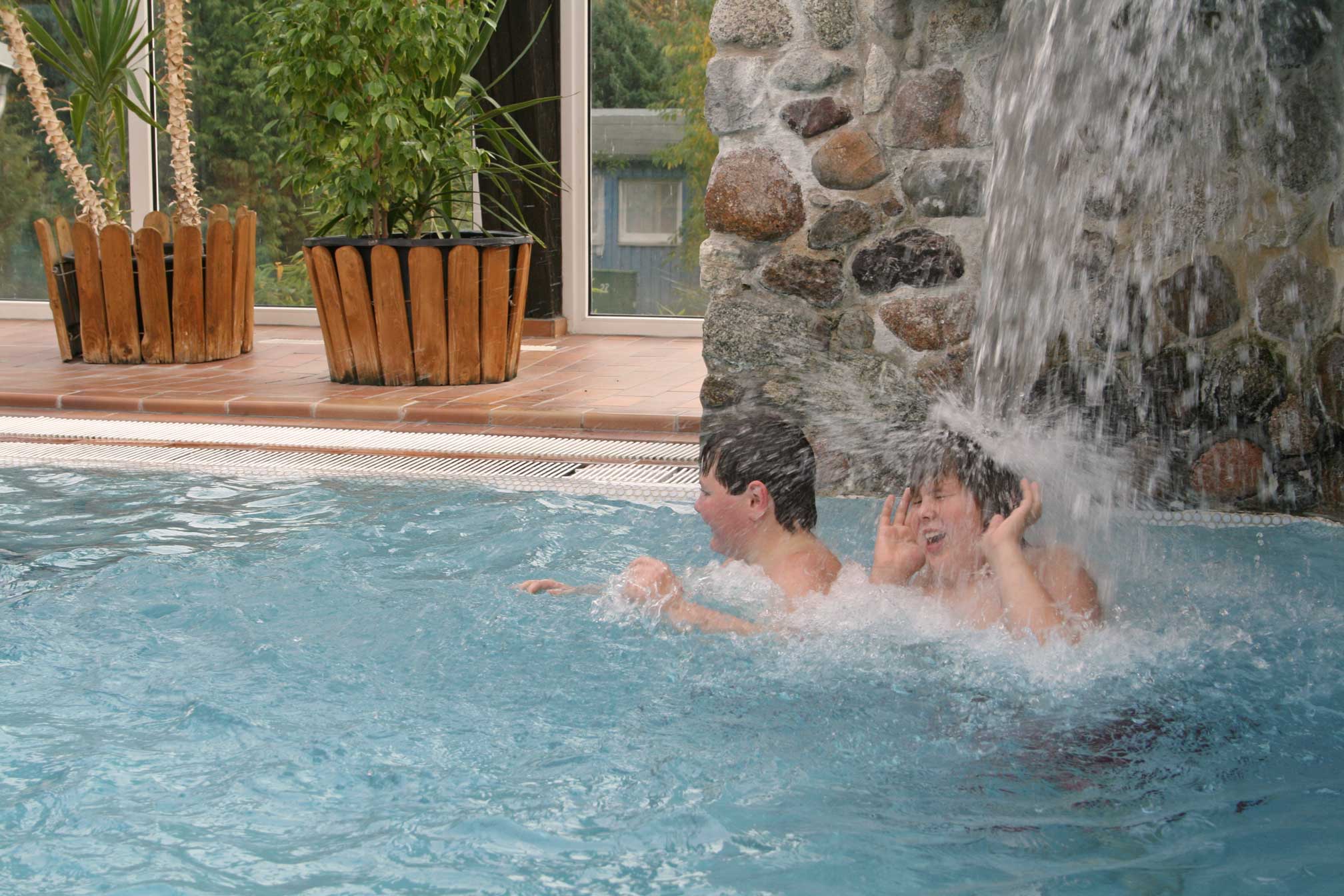 Foto von zwei Jungen, die unter einem Wasserfall im Schwimmbad stehen.