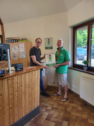Bild von der Geschäftsleitung des Ferienparks, der die Auszeichnung von dem Inspekteur von ACSI in der Rezeption entgegen nimmt.