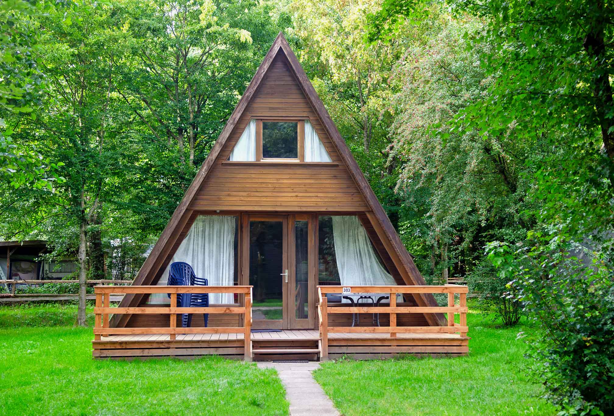 Typ E – Nurdachhaus 303 mit großer Terrasse, Holzelementen und Wiese drumherum, vor grünem Hintergrund