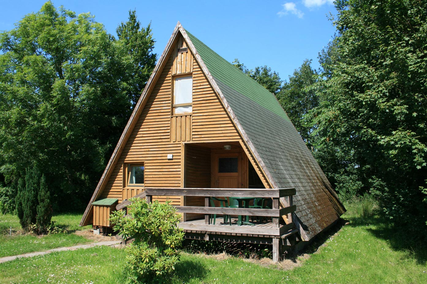 Typ C – Nurdachhaus 312 mit Holzfassade und Terrasse, eingebettet in grüner Wiese vor Bäumen