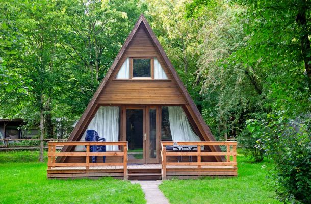 Typ E – Nurdachhaus 303 mit großer Terrasse, Holzelementen und Wiese drumherum, vor grünem Hintergrund