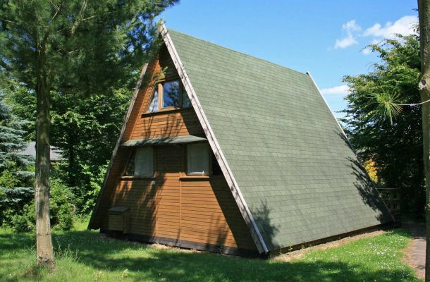 Typ E – Nurdachhaus 337 mit grünem Dach, Holzveranda und Wald im Hintergrund