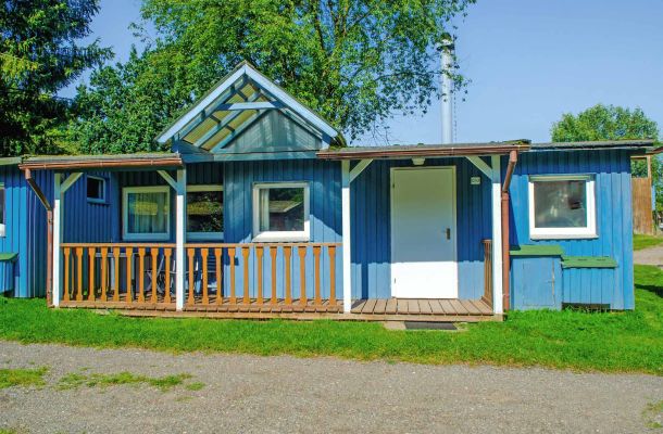 Typ A – Blaues Chalet 3 mit kleinem Holzbalkon und weißen Fensterrahmen, auf grünem Grundstück unter Bäumen