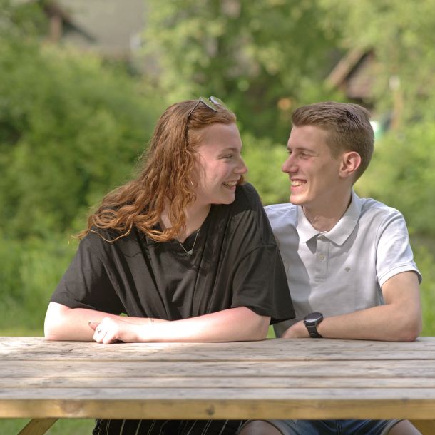 Foto eines jungen Paares, das an einem Holztisch sitzt. 