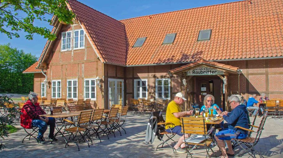 Foto der Terrasse vom Restaurant "Raubritter" mit Gästen, die vor dem Restaurant essen und trinken.