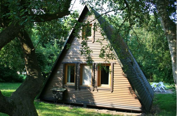 Typ B – Nurdachhaus 152 mit zentralem Eingang, dreieckiger Dachform und Holzverkleidung im Waldgebiet