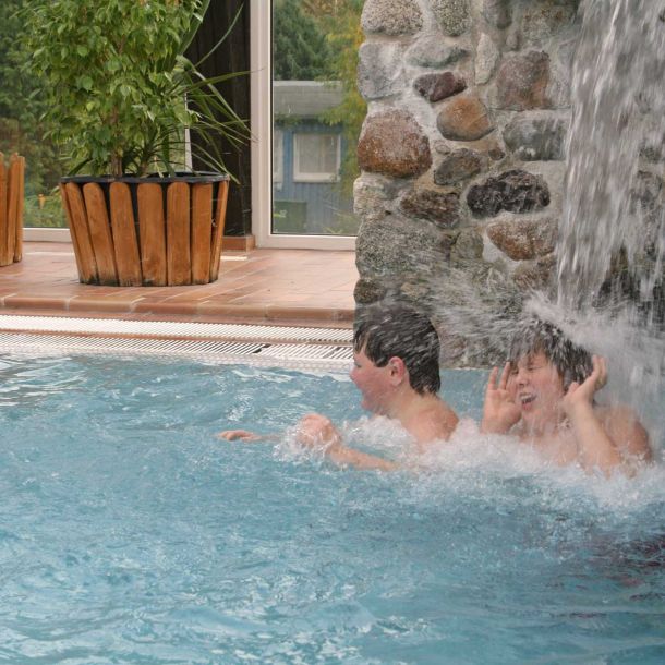 Foto von zwei Jungen, die unter einem Wasserfall im Schwimmbad stehen.