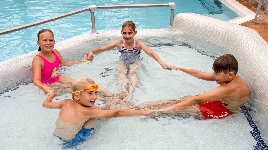 Foto von vier Kindern, die im Kinderbecken sitzen und sich an den Händen halten.