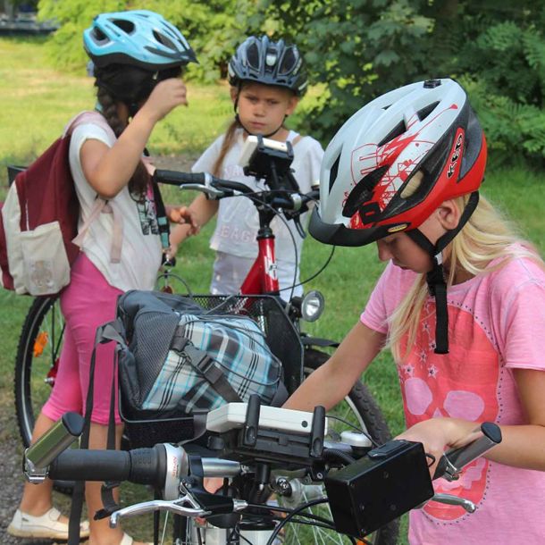 Foto von drei Mädchen mit Fahrrädern und Fahrradhelmen auf einer Wiese.