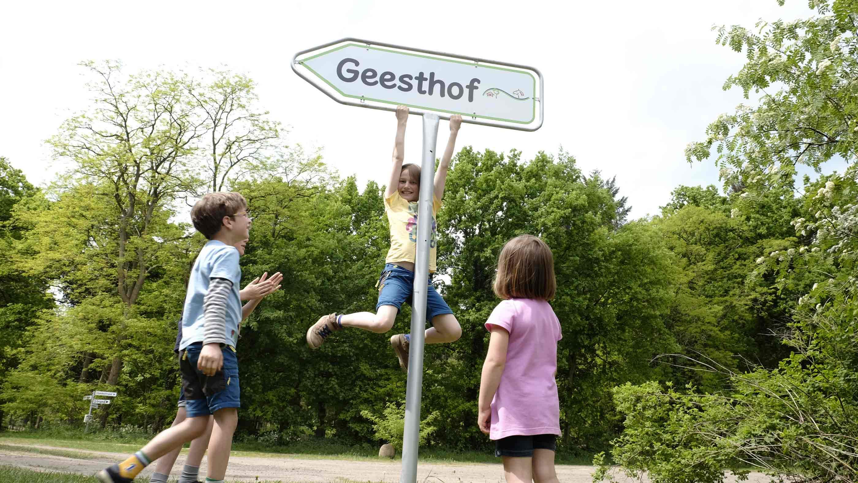 Foto eines Metallschildes mit der Aufschrift "Geesthof" an dem ein Kind hangelt