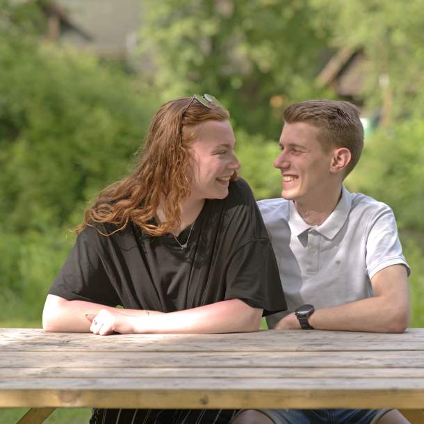 Foto eines jungen Paares, das an einem Holztisch sitzt.