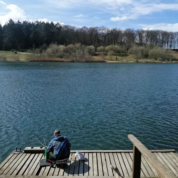 Foto eines jungen Anglers, der auf dem Steg des Geestsees hockt und an seiner Angel arbeitet.