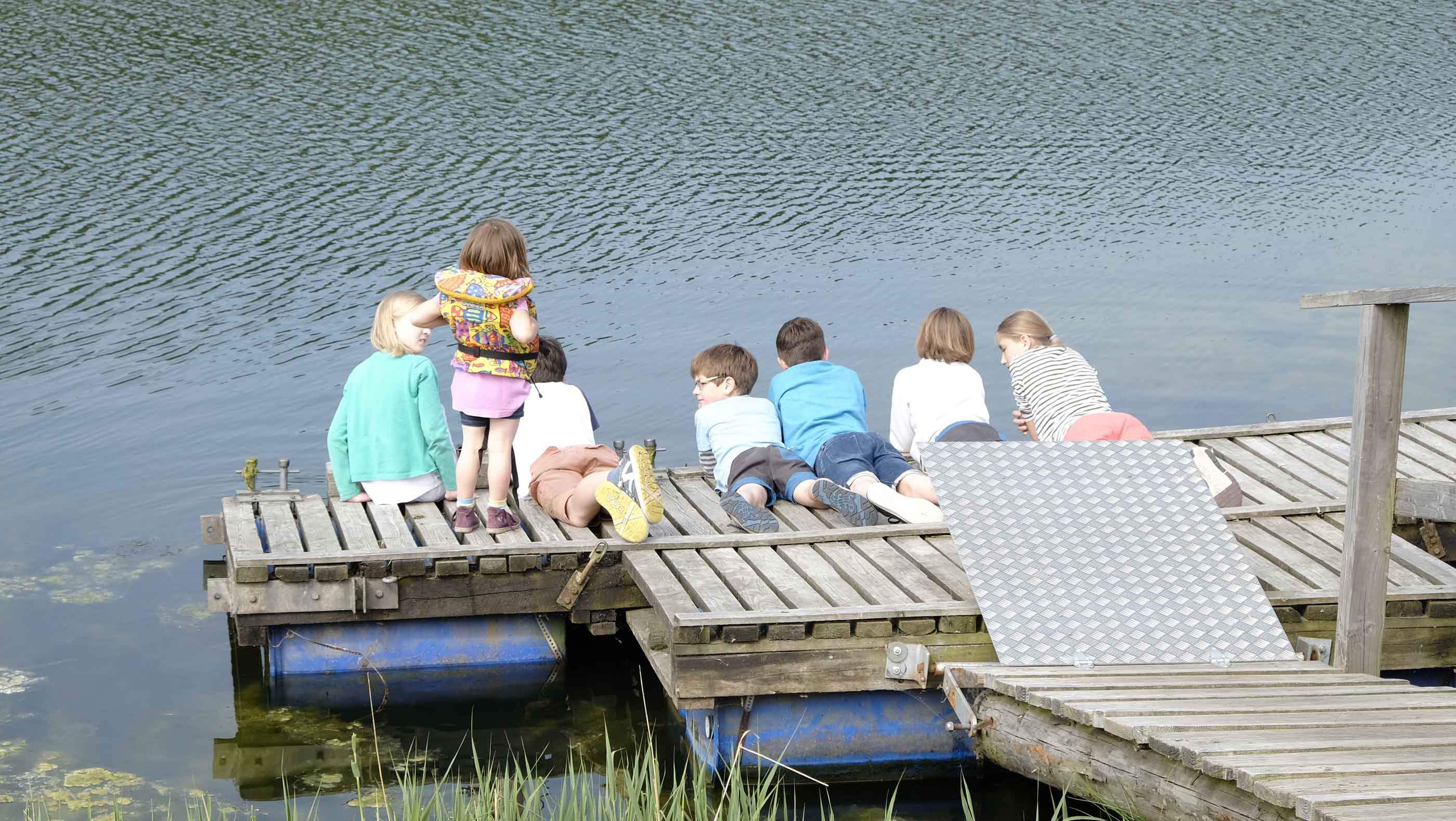 Foto von mehreren Kindern auf einem Holzsteg am Wasser
